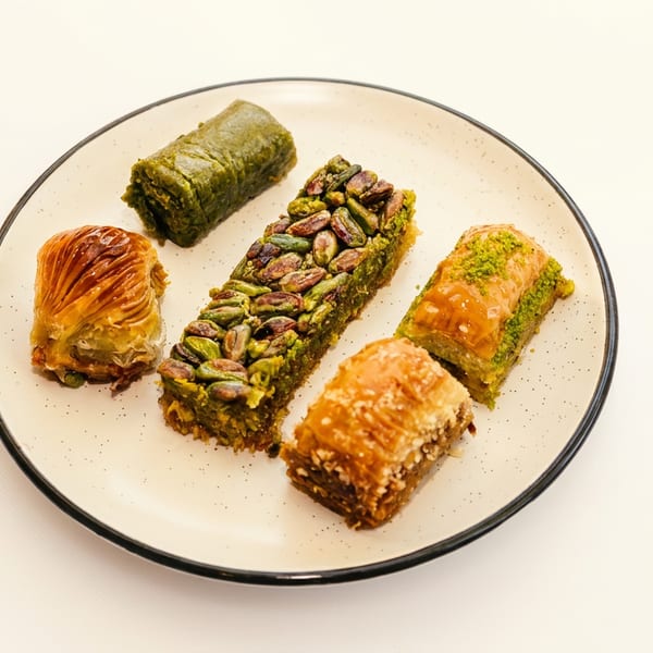 A white plate holds five pieces of baklava, some topped with pistachios, on a white background.