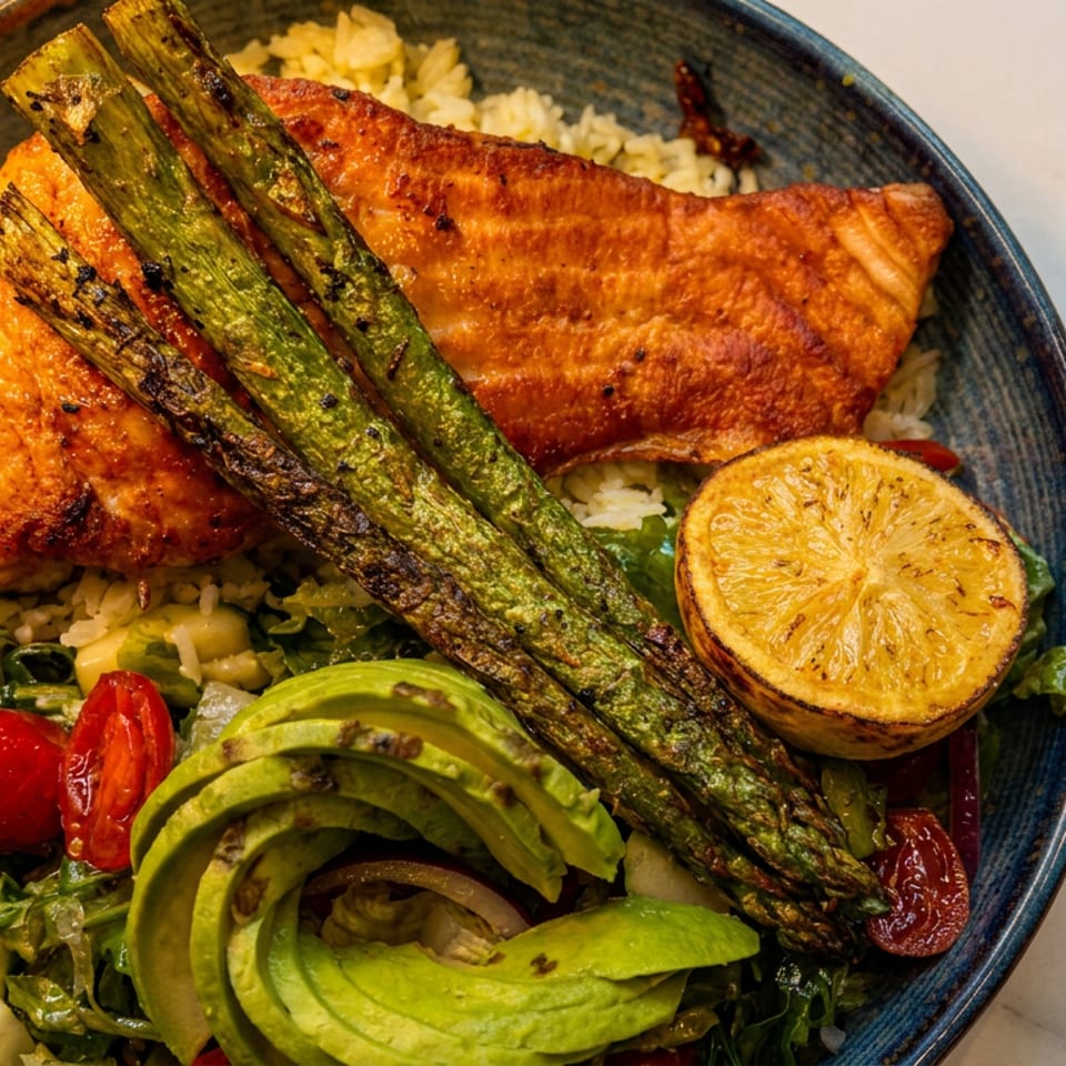 Grilled salmon with asparagus, avocado, cherry tomatoes, and lemon over rice in a blue bowl.